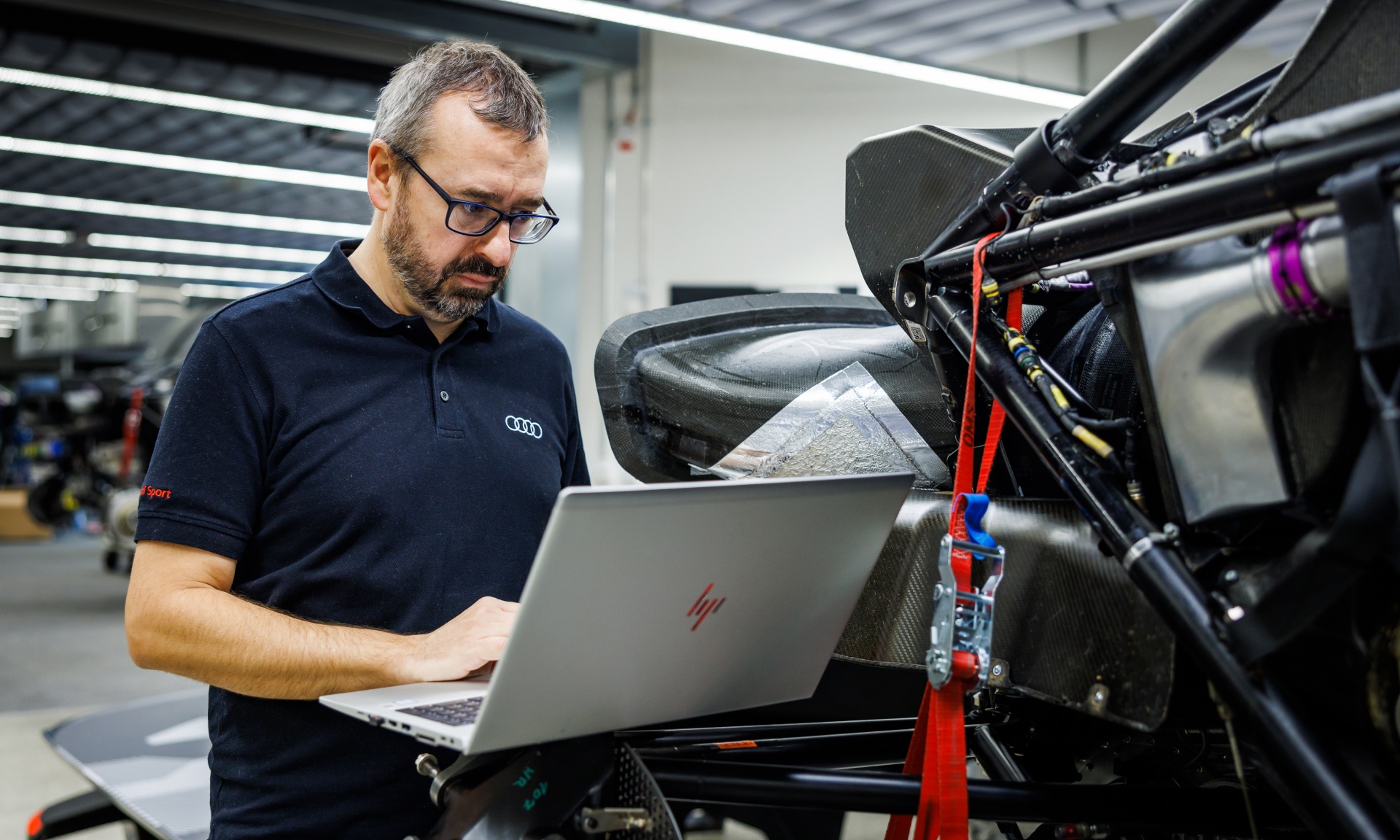 Arnau Niubó Bosch in einer Arbeitssituation am Computer neben dem demontierten Audi RS Q e-tron. 