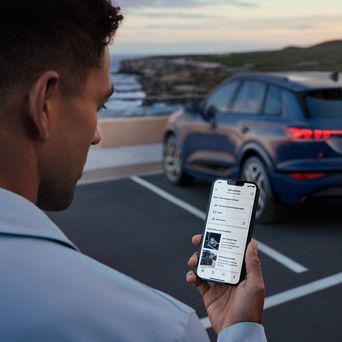 Mann mit Handy in der Hand steht vor einem Audi Q4