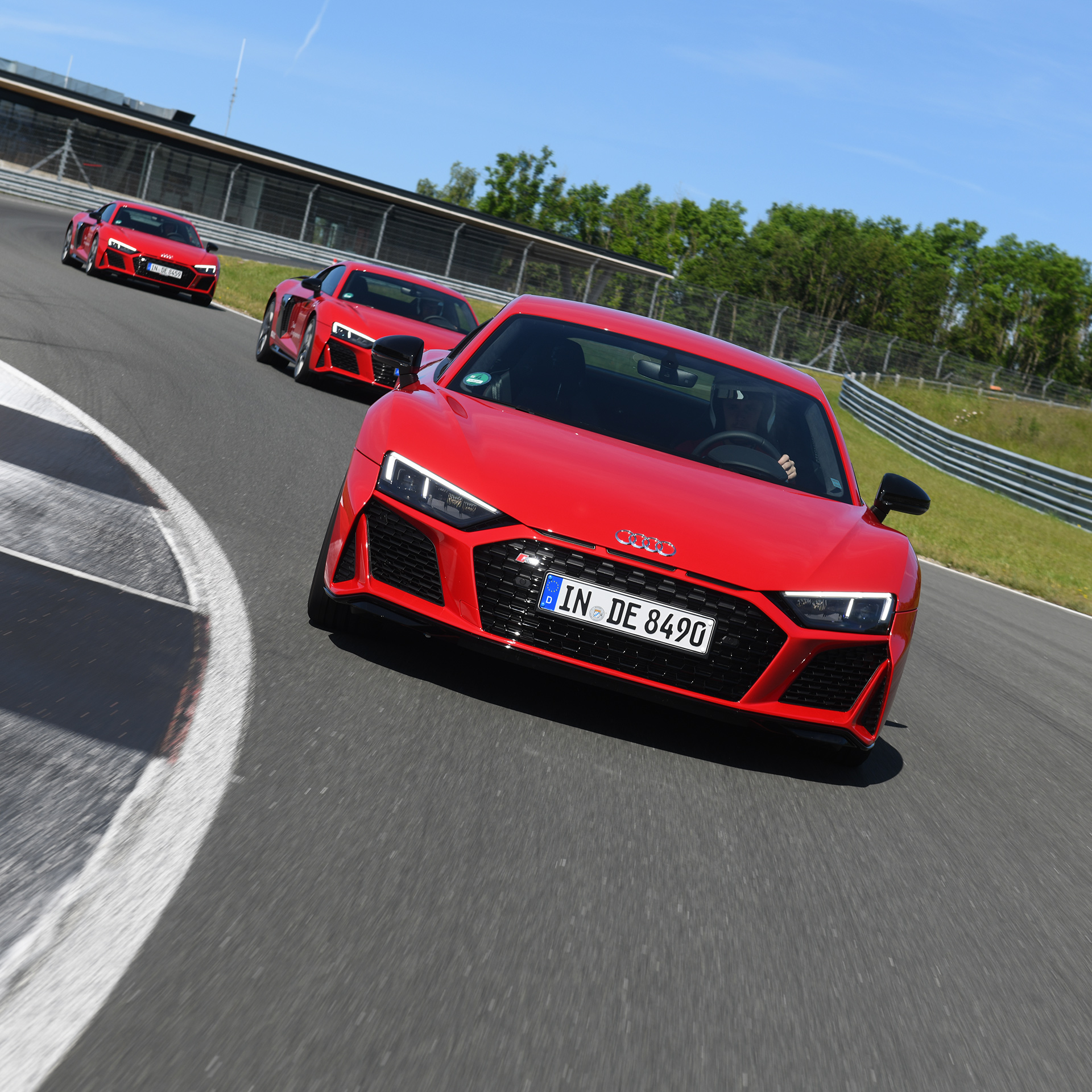 Three red Audi R8 models drive one after another on a race track